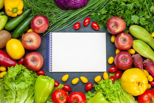 Top view vegetables and fruits lettuce tomatoes cucumber dill cherry tomatoes zucchini green onion parsley apple lemon kiwi notebook in center