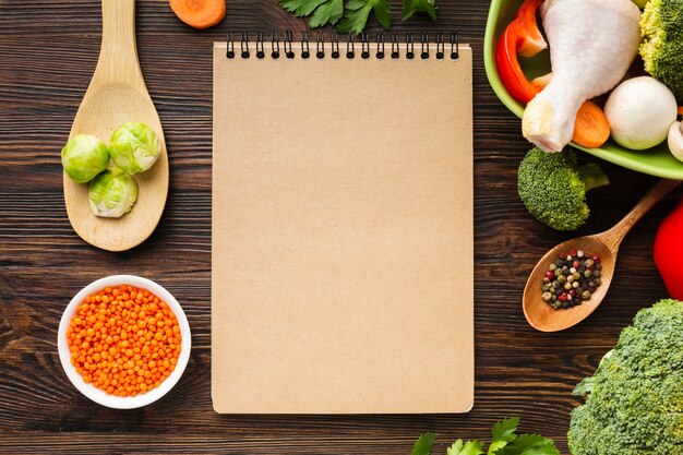 Top view vegetables mix and chicken drumstick in bowl with blank notebook