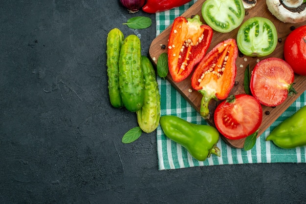 Free photo top view vegetables mushrooms cut tomatoes bell peppers on cutting board cucumbers on black table