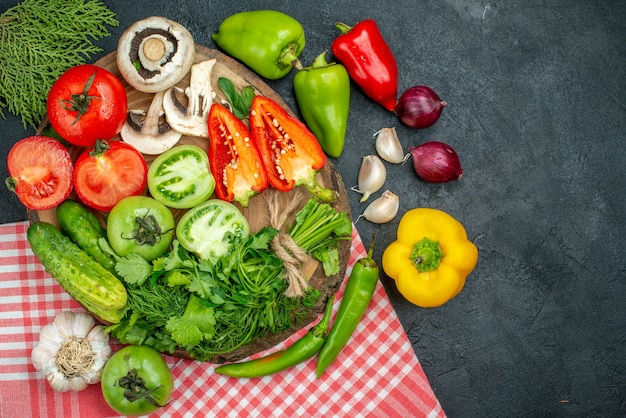 Top view vegetables mushrooms red and green tomatoes bell peppers greens on rustic board red onions hot peppers garlic red white checkered tablecloth on black table