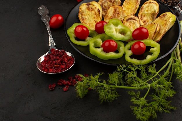 top view vegetables sliced and whole inside black plate along with greens on the dark background