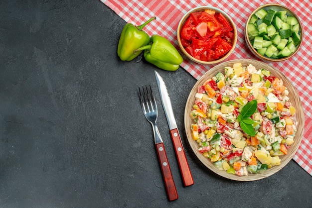 その下に赤いナプキンと野菜が横にあるカトラリーと濃い灰色の背景にテキストの場所とボウルの野菜サラダの上面図