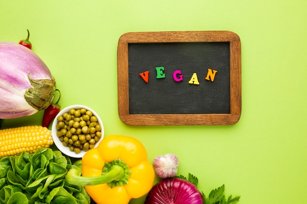 Free photo top view veggies on green background with vegan lettering