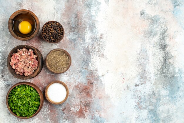 Top view vertical row bowls with meat greens egg yolk pepper powder black pepper salt on nude surface free space