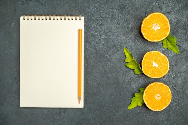 Top view vertical row cut oranges a notebook and pencil on dark background