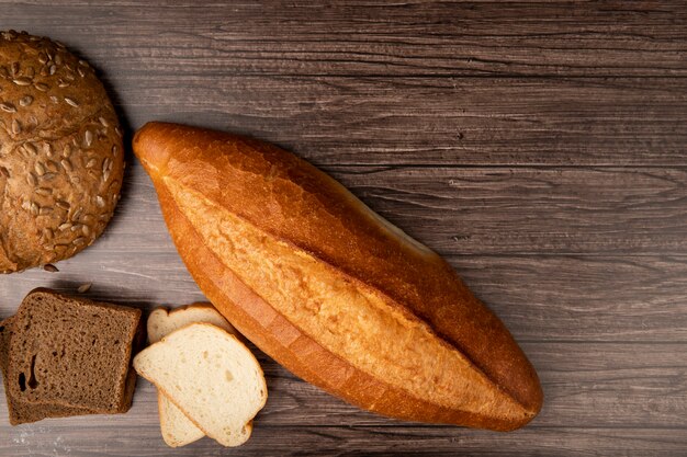Top view of vietnamese baguette with rye and white bread slices cob on left side and wooden background with copy space