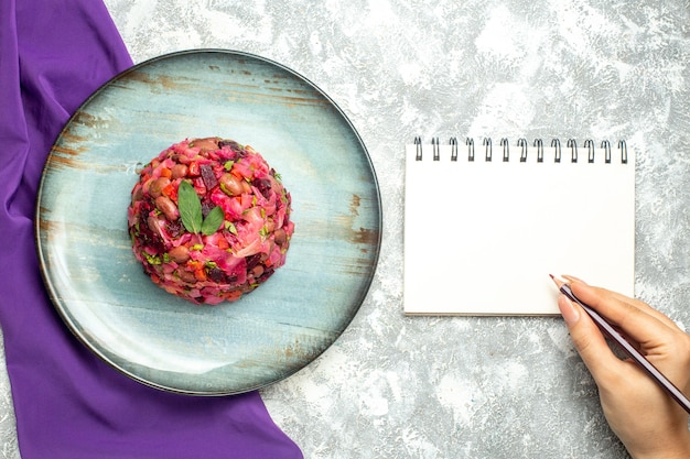 Бесплатное фото Вид сверху винегрет картофельный салат на круглой тарелке фиолетовый шаль блокнот карандаш в женской руке на светлом столе