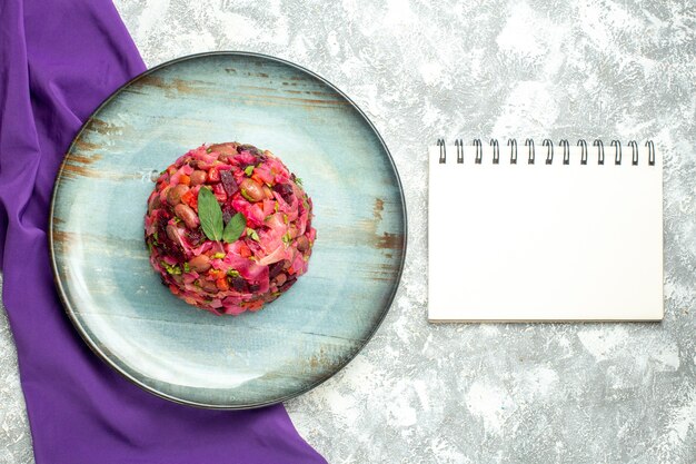 Top view vinaigrette beet potato salad on round plate purple shawl notebook on light table