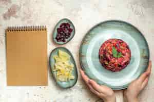 Free photo top view vinaigrette salad on oval plate in female hand cut beet and other stuff in bowls on light grey table