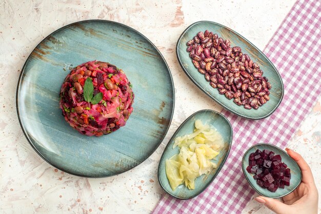 Top view vinaigrette salad on plate pickled cabbage beans cut beet on plates beet plate in woman hand on light grey table