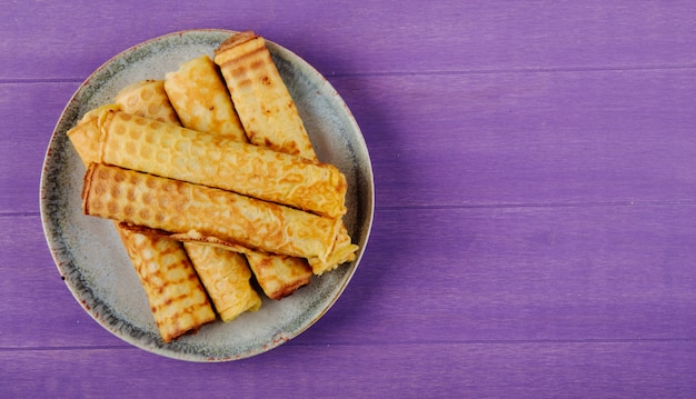 Top view of wafer roll filled with condensed milk on a plate on wooden purple background with copy space