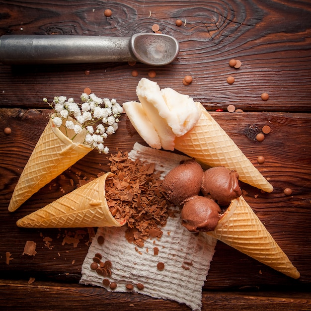 Top view waffle cones with chocolate ice-cream and vanilla ice cream and chocolate chips and ice cream spoon in rag napkins