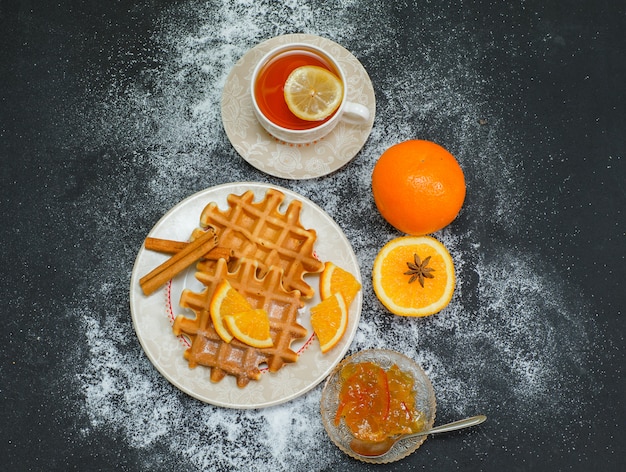 Top view waffle in plate with tea, orange, lemonnd jam on dark. horizontal