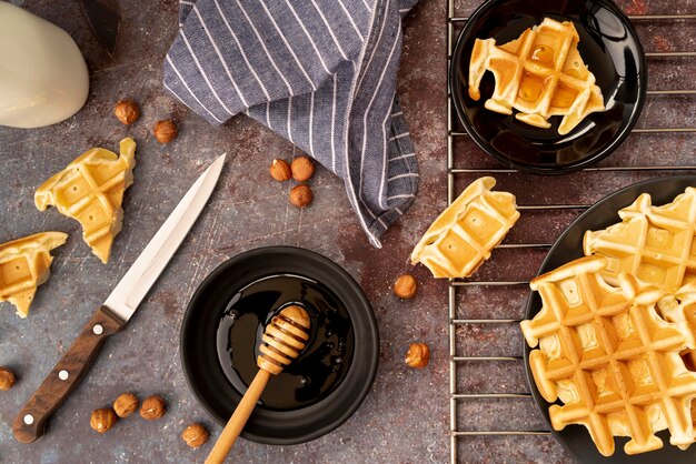 Top view of waffles covered in honey with hazelnuts and honey dipper