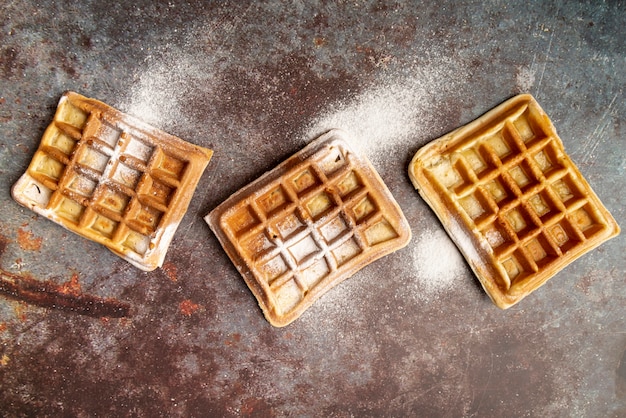 Top view of waffles on rusty surface covered in powdered sugar