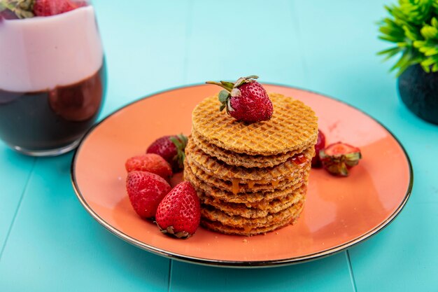 Top view of waffles with fresh strawberries on an orange plate on blue surface