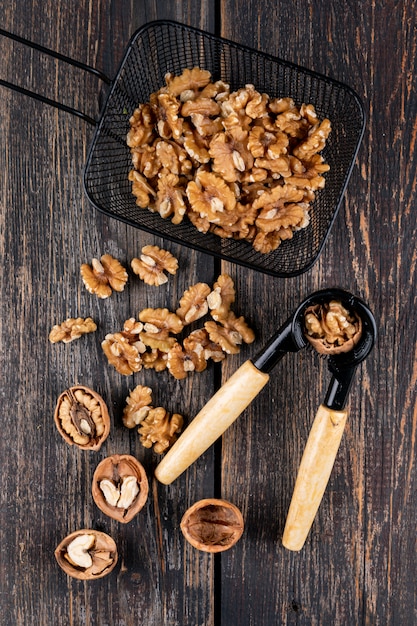 Top view walnuts in black basket with nutcracker on wooden  vertical