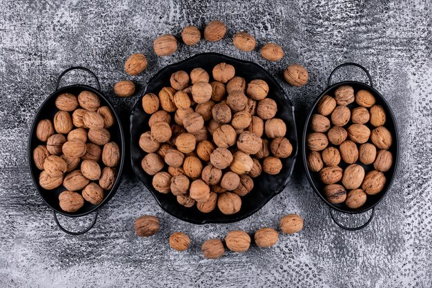 Вид сверху грецкие орехи в черных корзинах и тарелка на деревянный стол горизонтальный