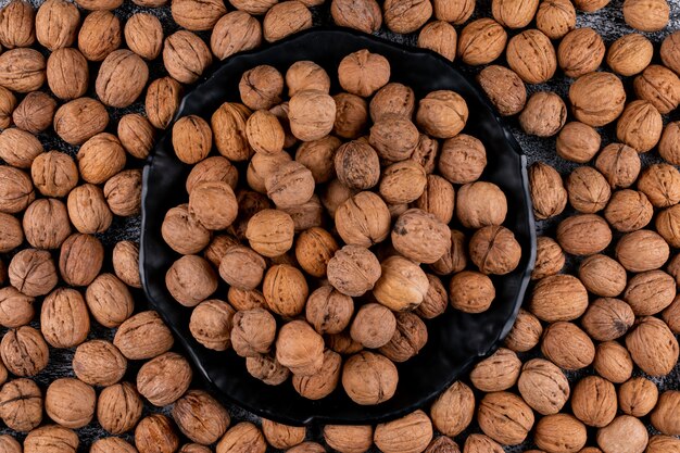 Top view walnuts in black plate surrounded by walnuts horizontal