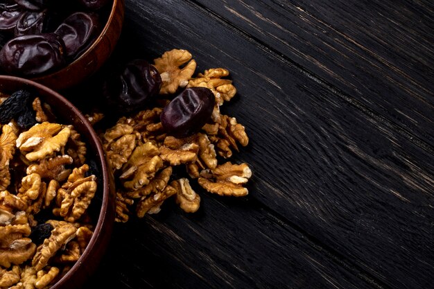 Top view of walnuts in a bowl and sweet dried date fruit on wooden