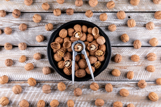 Free photo top view walnuts in bowl with nutcracker on wooden  horizontal