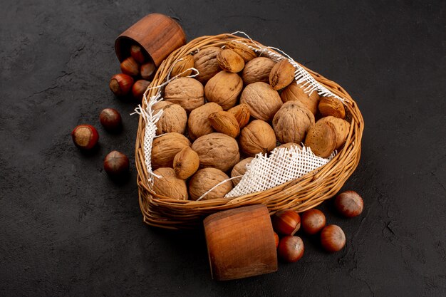 top view walnuts and hazelnuts inside basket and brown pot on the dark background