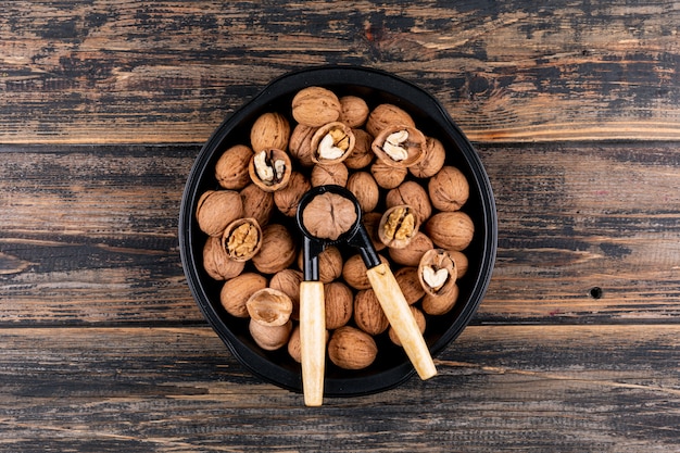 Top view walnuts and nutcracker in plate on wooden table horizontal