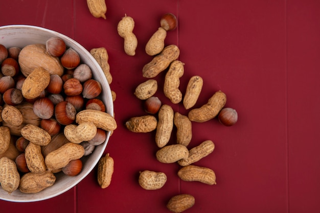 Вид сверху грецкие орехи с фундуком и арахисом в миске на красном столе