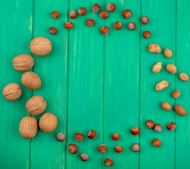 Top view of walnuts with hazelnuts and peanuts on a green surface