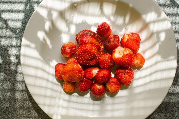 Top view of washed and cleaned ripe strawberries in a simple white bowl on the table indoors. Healthy food concept