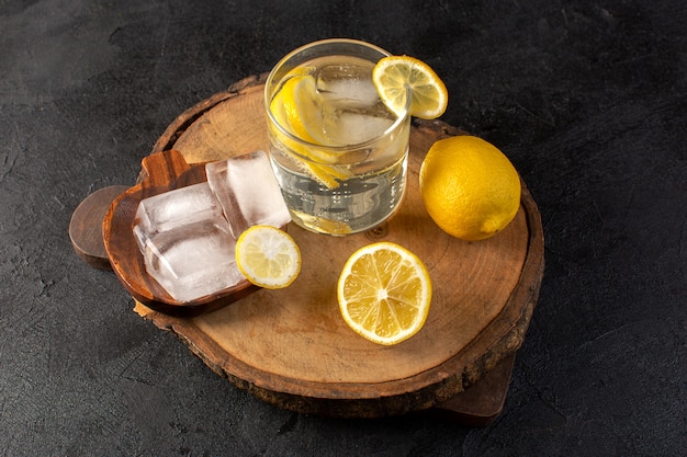 A top view water with lemon fresh cool drink inside glass with ice cubes with sliced lemons on the dark background cocktail drink fruit