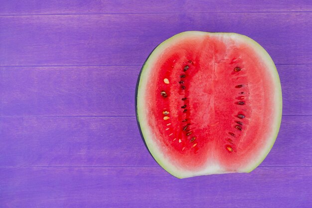 Top view of watermelon half on right side and purple background with copy space
