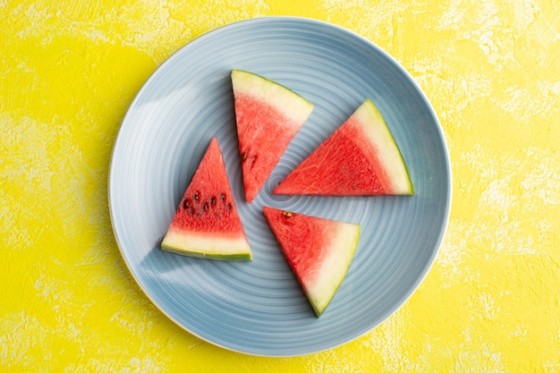 Top view of watermelon slices inside blue plate on the yellow desk