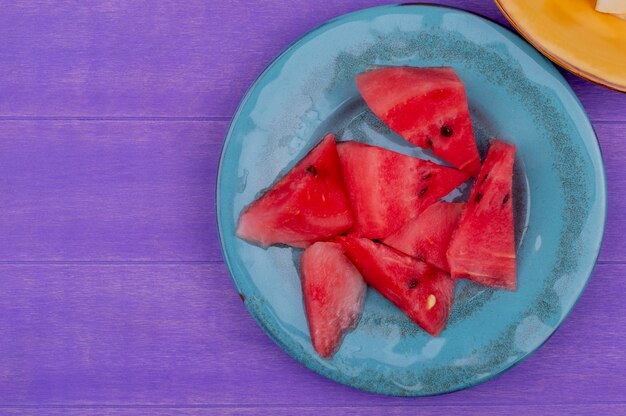 Top view of watermelon slices in plate on purple background with copy space