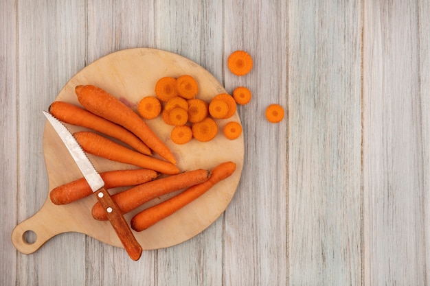 Top view of weight-loss-friendly food carrots on a wooden kitchen board with knife with chopped carrots on a grey wooden wall with copy space