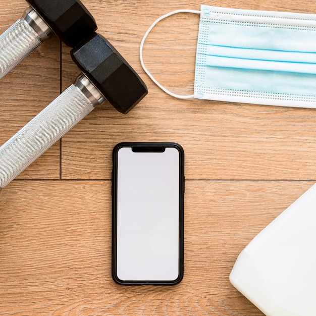 Top view of weights with smartphone and medical mask