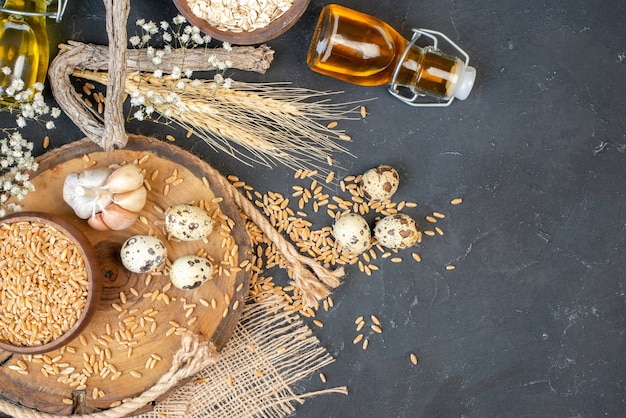 Вид сверху зерна пшеницы в миске, чеснок на натуральной деревянной доске, бутылка масла для перепелиных яиц на столе, место для копирования