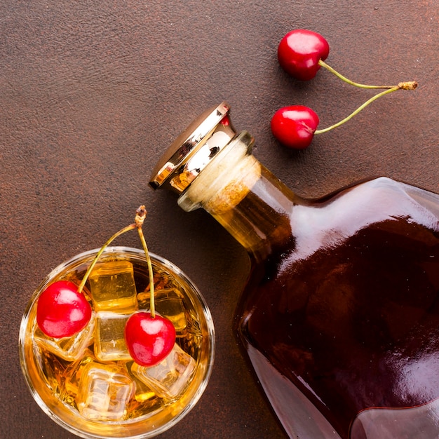 Vista dall'alto bicchiere di whisky e ciliegie con bottiglia