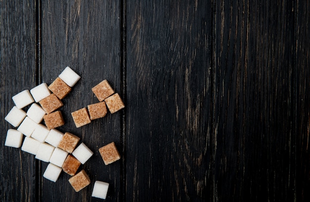 La vista superiore dei cubi dello zucchero bianco e marrone ha sparso su fondo di legno scuro con lo spazio della copia