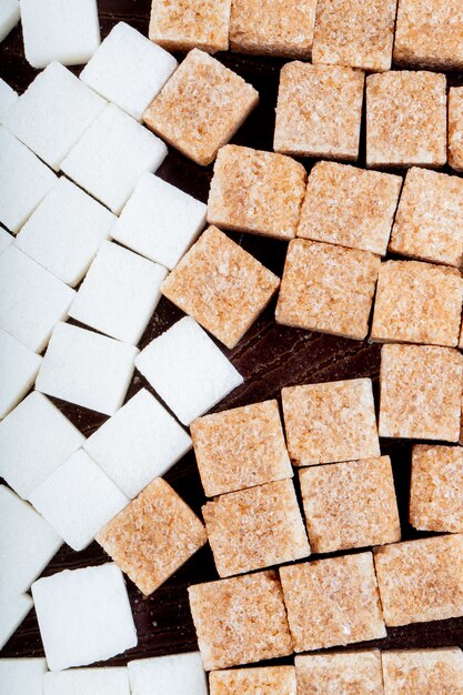 Top view of white and brown sugar cubes scattered on dark wooden background