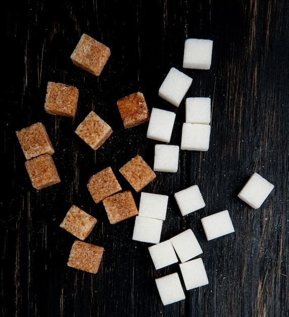 Top view of white and brown sugar cubes scattered on dark wooden background