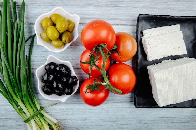 Вид сверху белого сыра со свежими помидорами, зеленым луком и маринованными оливками