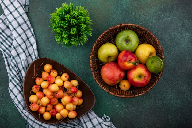 Top view white cherry in a bowl with apples in a basket on a green table