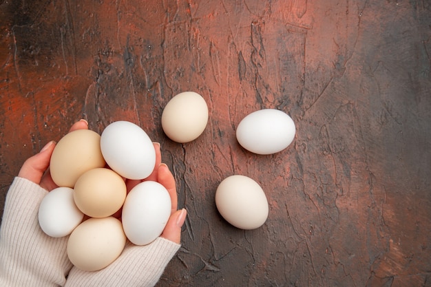 Вид сверху белые куриные яйца в женских руках на темном столе