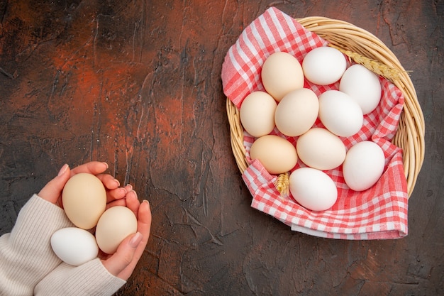 Top view white chicken eggs inside basket with towel on a dark table