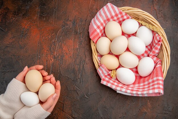 暗いテーブルの上のタオルとバスケットの中の白い鶏卵の上面図