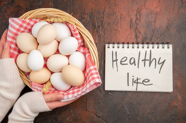 Top view white chicken eggs inside basket with towel on dark table