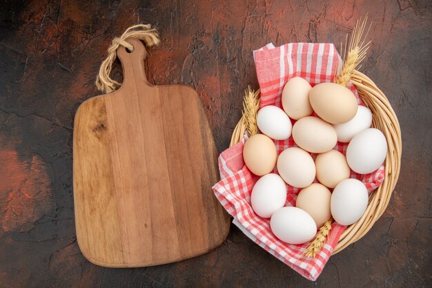 Top view white chicken eggs inside basket with towel on dark table