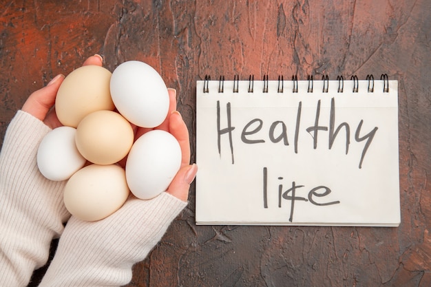 Free photo top view white chicken eggs inside female hands on dark table