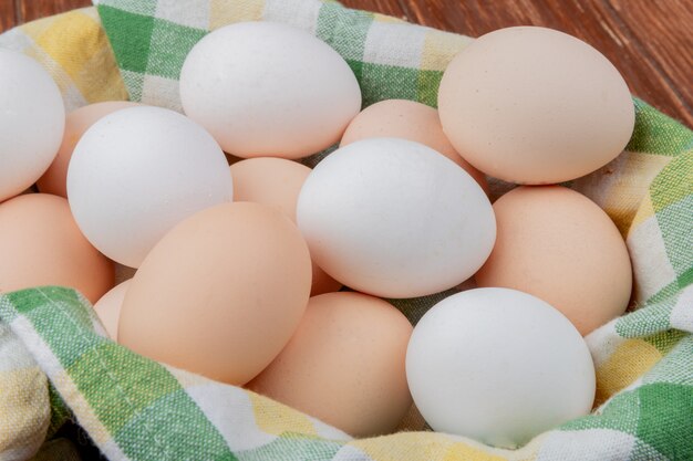 Top view of white and cream colored chicken eggs on a checked tablecloth on a wooden background